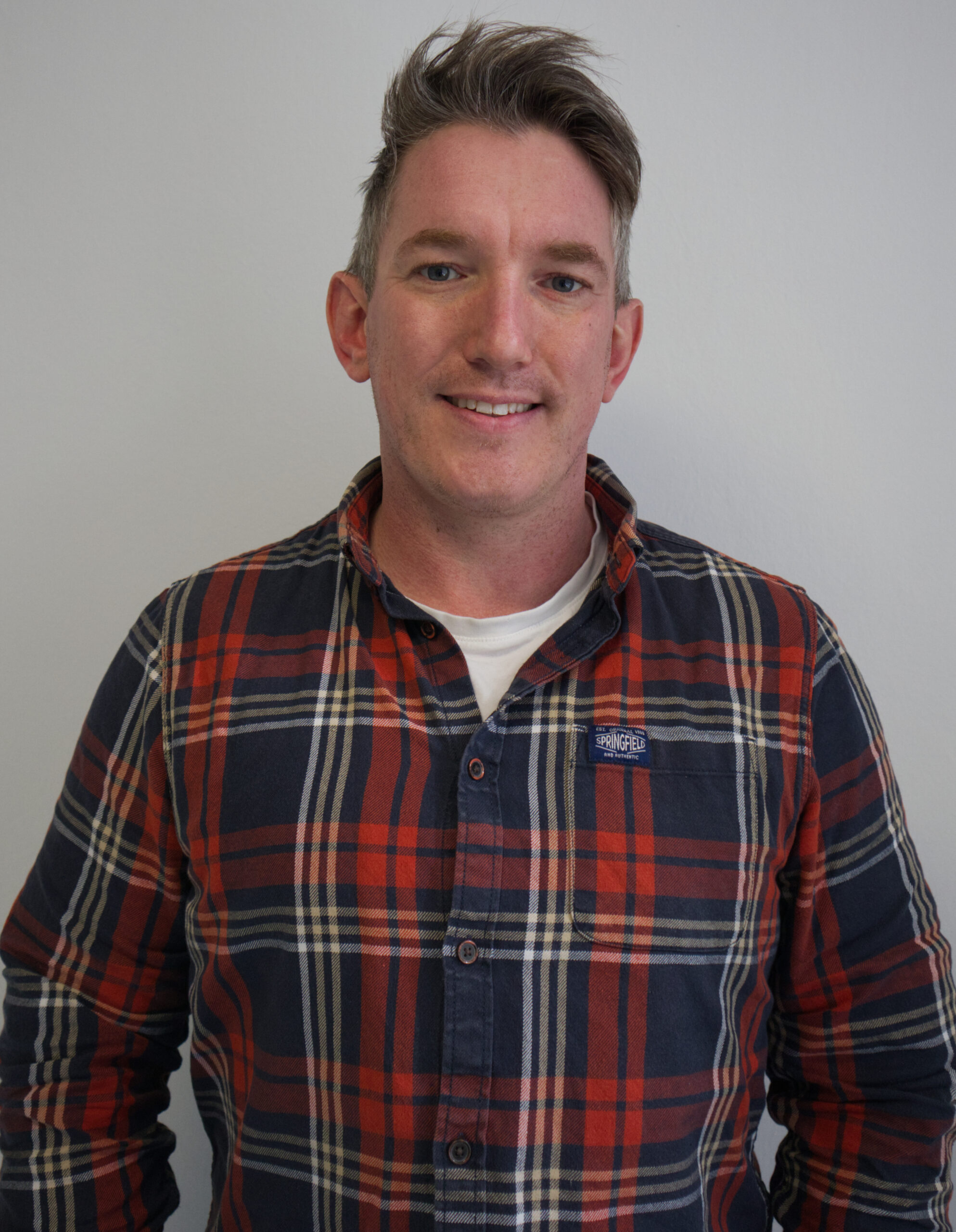 a portrait photo of Jamie Coles, wearing a chequed shirt on a white background